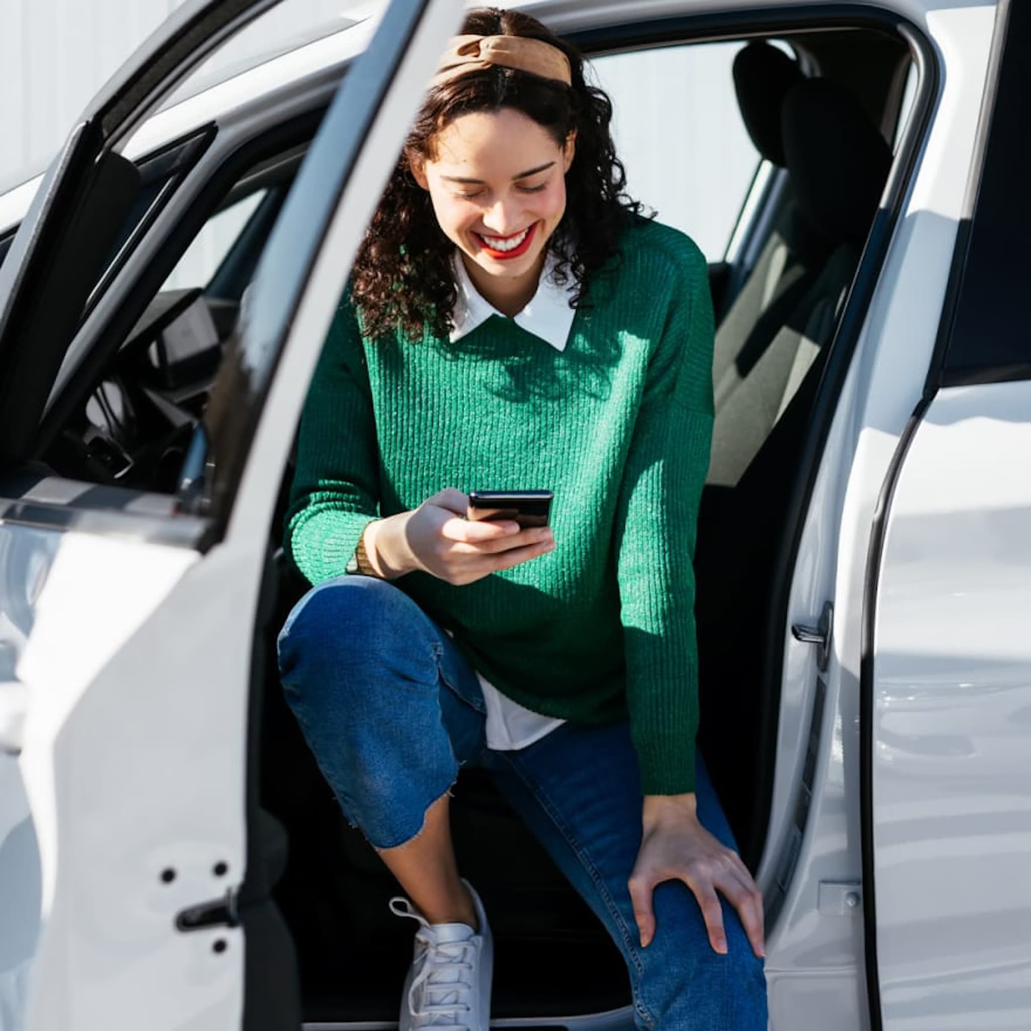 Frau sitzt in einem Auto und nutzt ihr Smartphone, um mit Autoeinfachlos eine Alternative zu „Wir kaufen dein Auto“ zu finden.